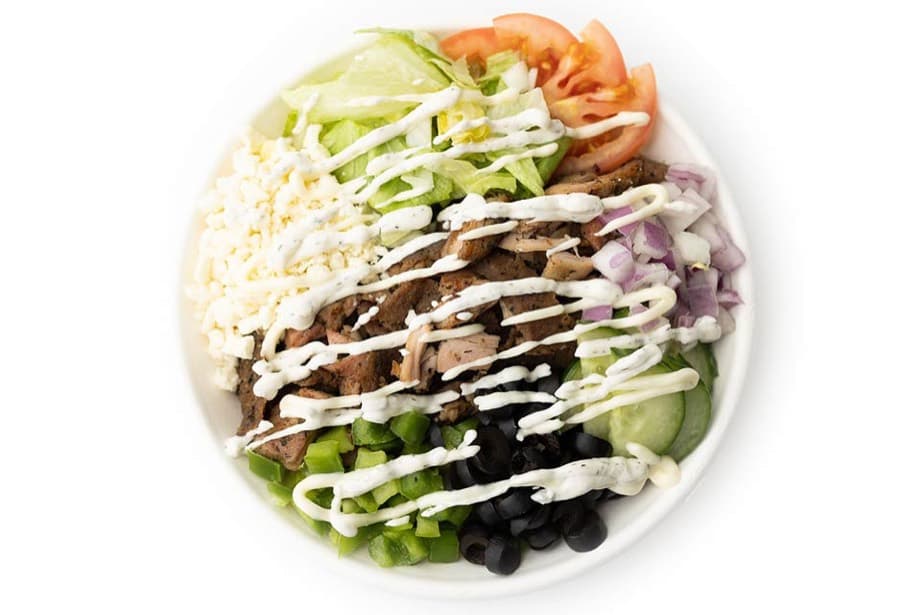 A rice bowl topped with carved donair meat, feta, lettuce, tomato, cucumber, red onion and olives.