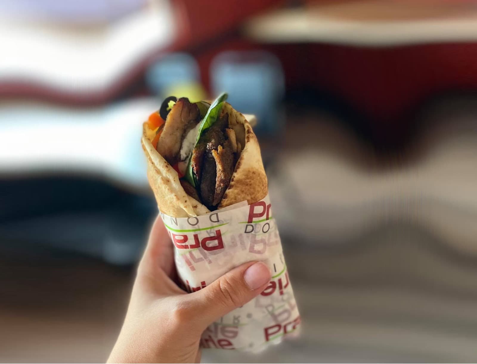 A Prairie Donair donair — grilled seasoned beef, fresh vegetables and sauce folded into warm flatbread — held in hand in branded wrapping paper.